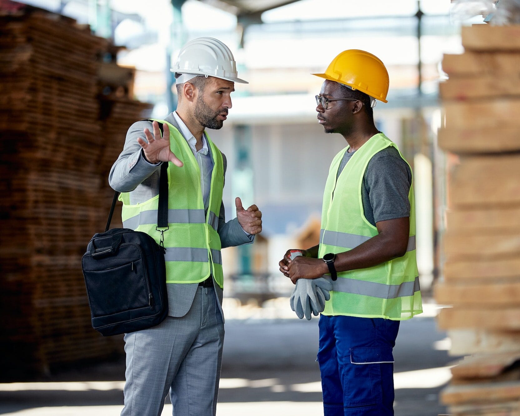 Warehouse manager talking to black worker at lumber distribution department.